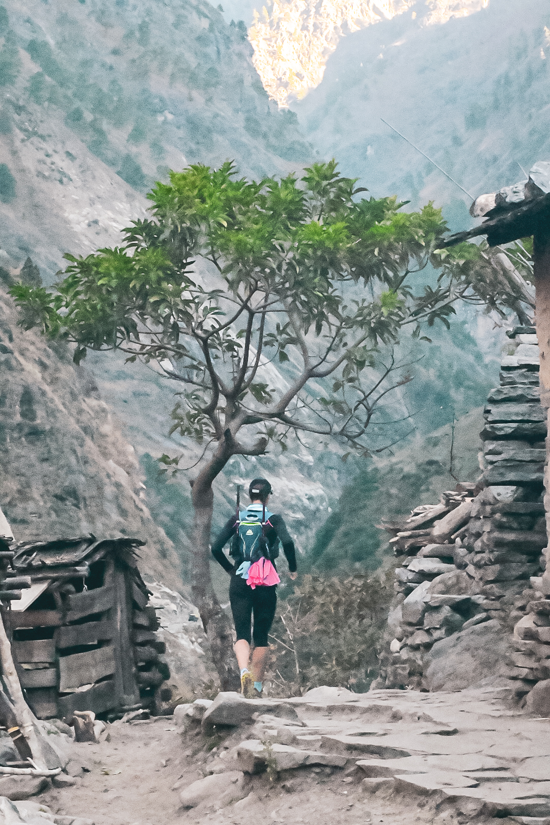 Trail runner heading into a mountain village on a stone path, surrounded by high peaks and morning mist