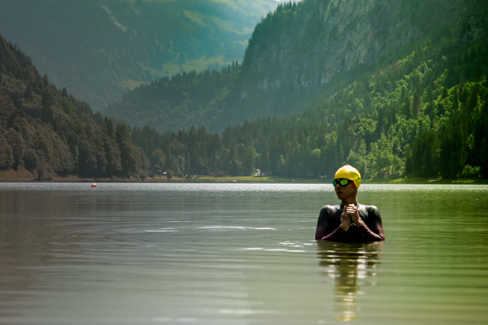 Swimmer in a yellow cap standing chest deep in an alpine lake before a race